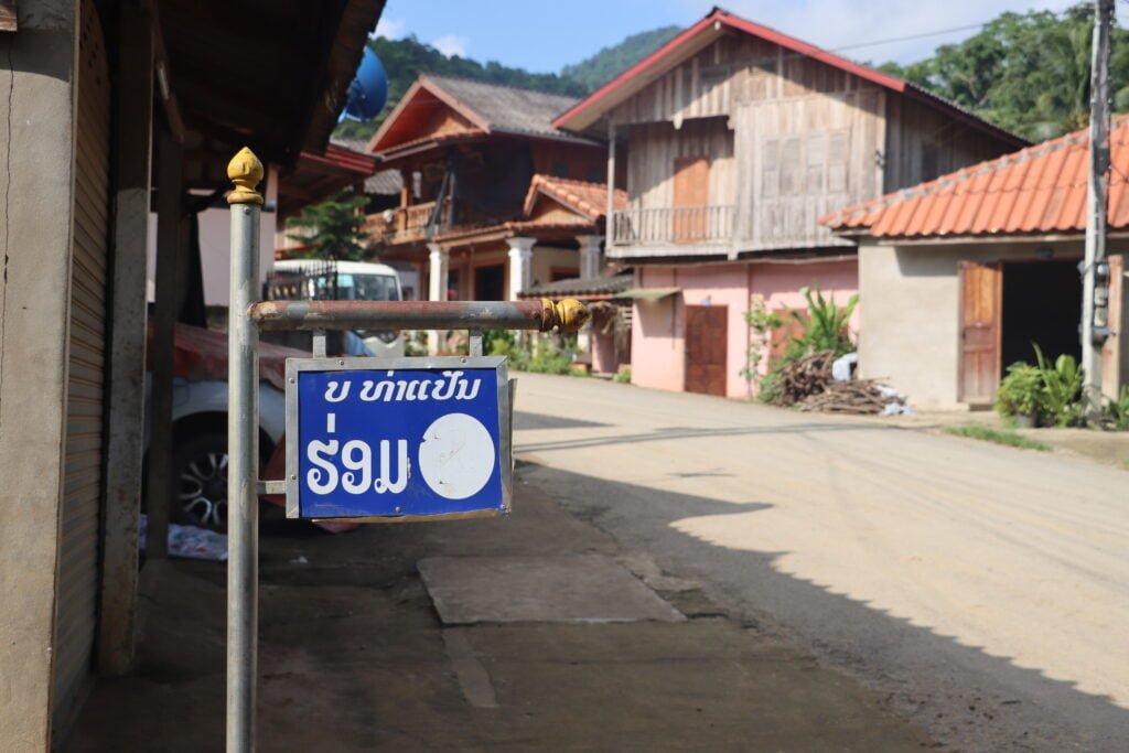 Le panneau dans la rue du village de Ban Thapene avec des maisons laotiennes en fond