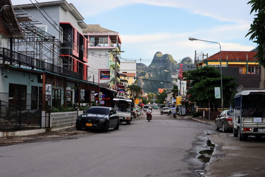 Une rue de la ville de Vang Vieng bordée de bâtiments colorés, de restaurants et de montagnes karstiques en arrière-plan.